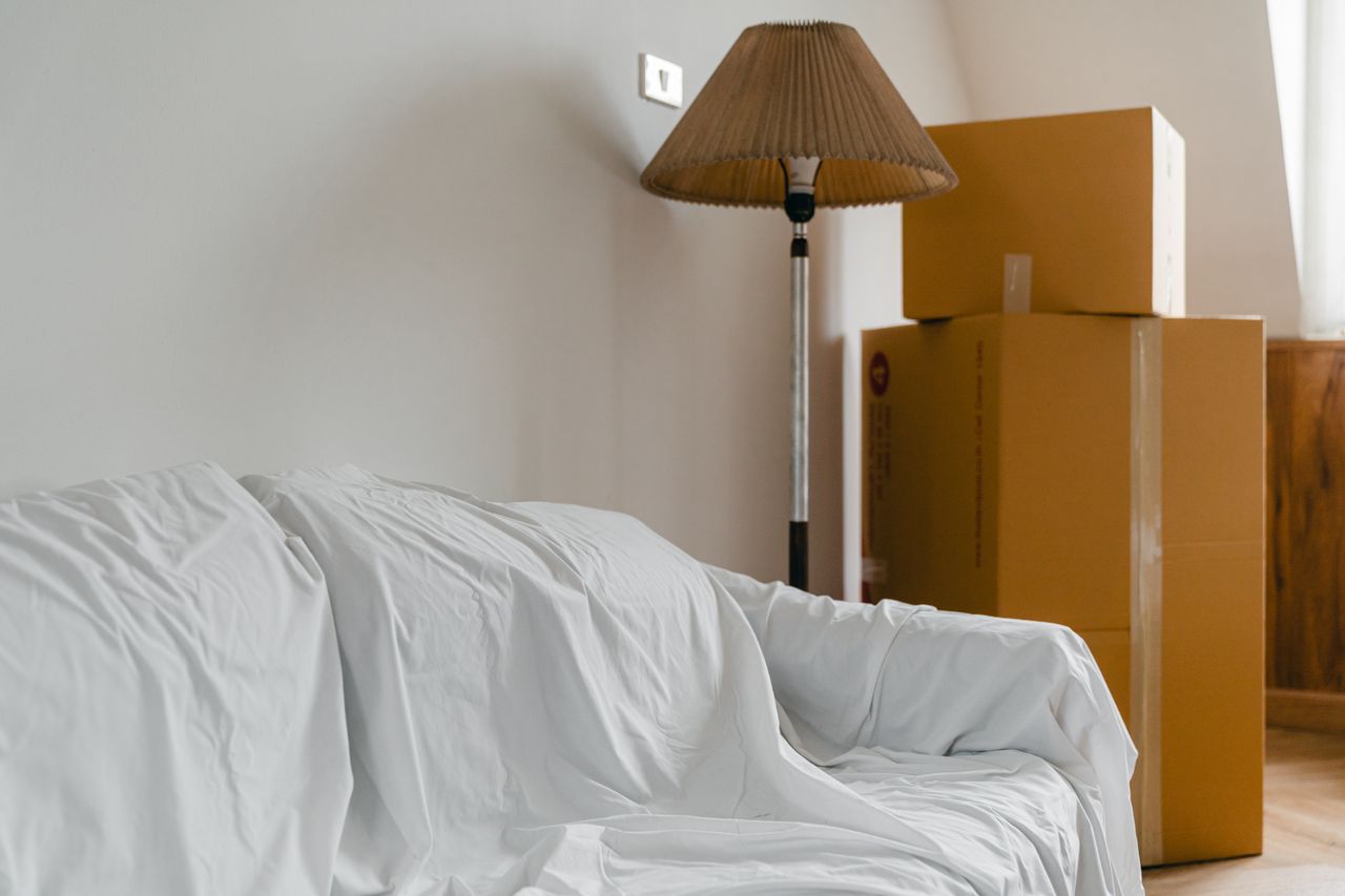 hero-img-01 A sheet-covered sofa and floor lamp, along with packed cardboard boxes, in the bright, spacious room of a new contemporary house
